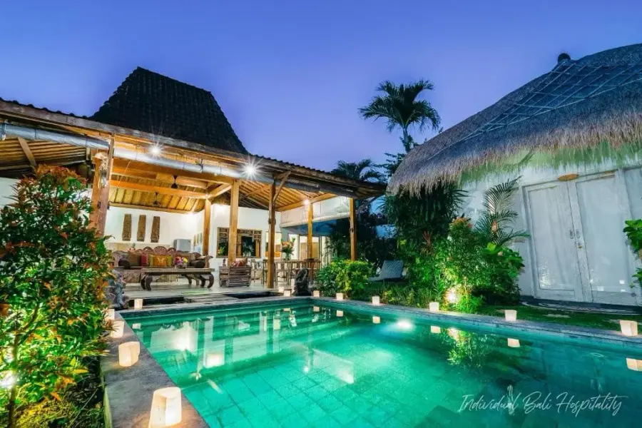 Villa Aniri at dusk — the pool lit by floating candles before the open Joglo pavilion