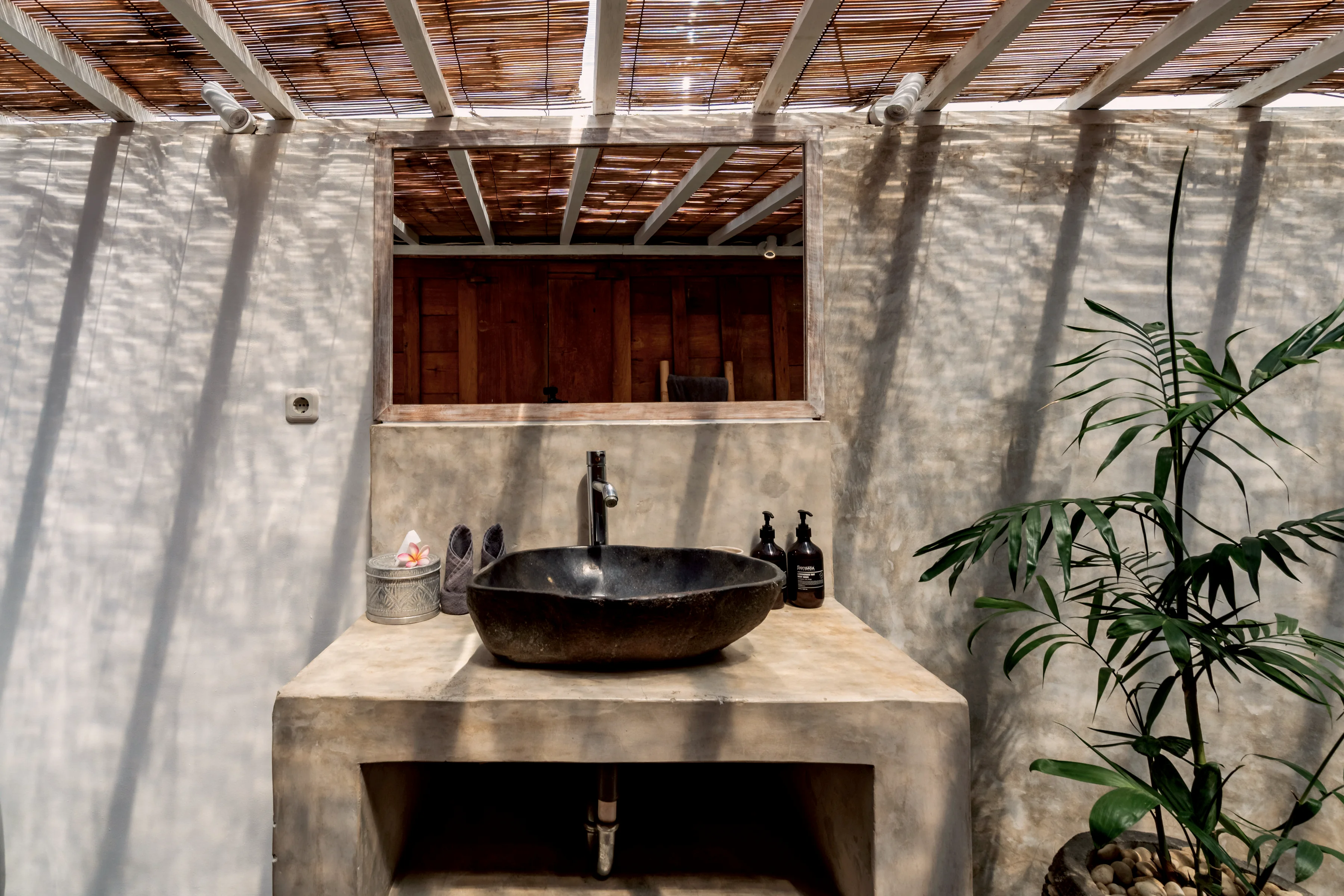 A dark stone basin on a concrete vanity, with plants under an open roof