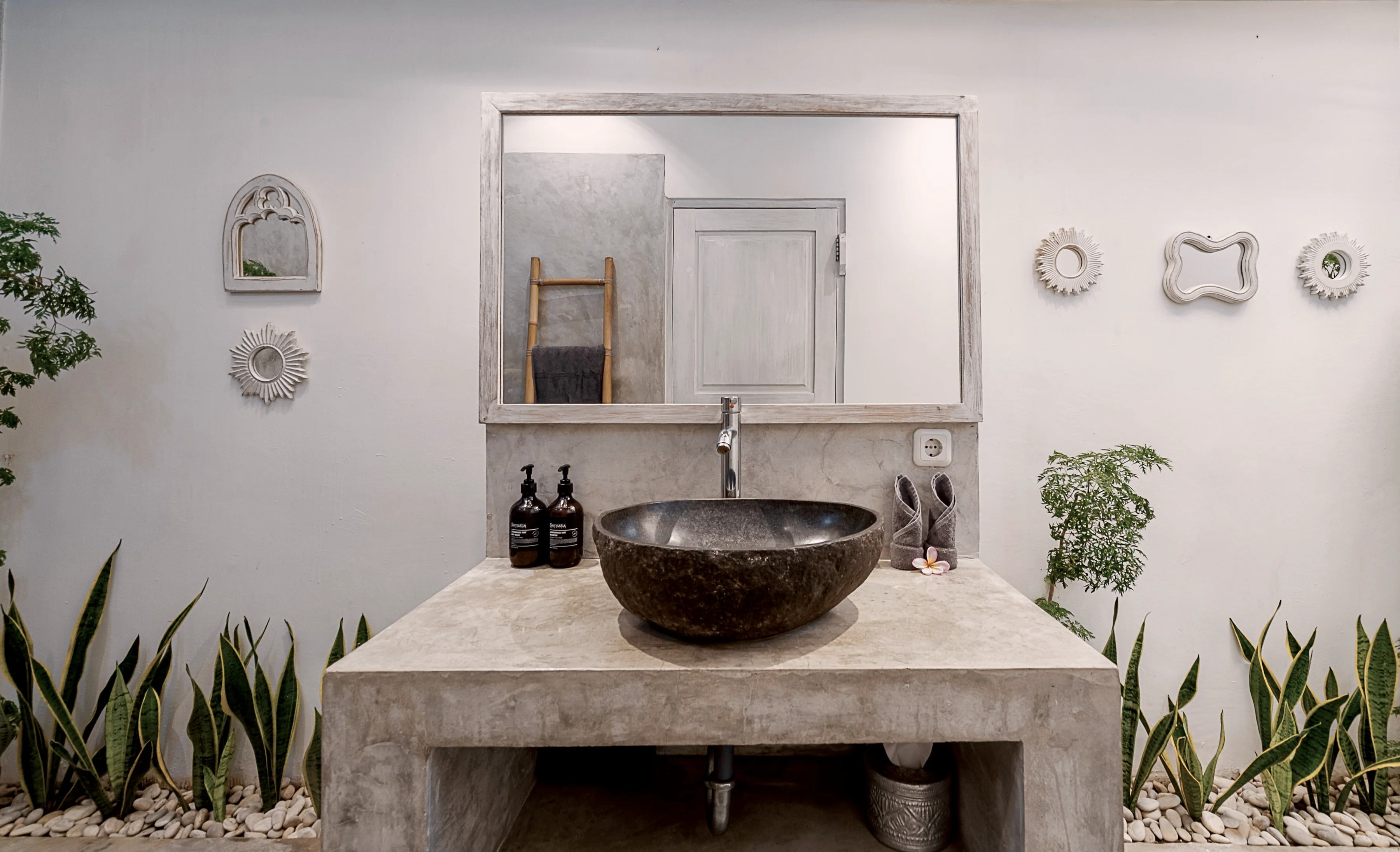 A stone basin on a concrete vanity under a round mirror