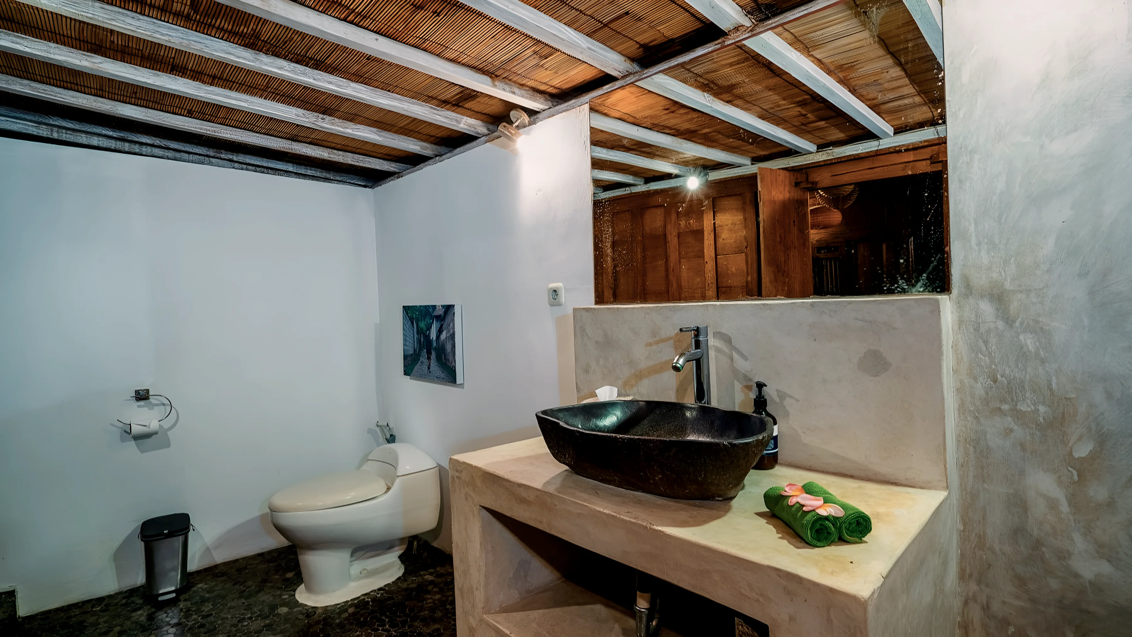 An open bathroom under a timber ceiling, with a stone basin