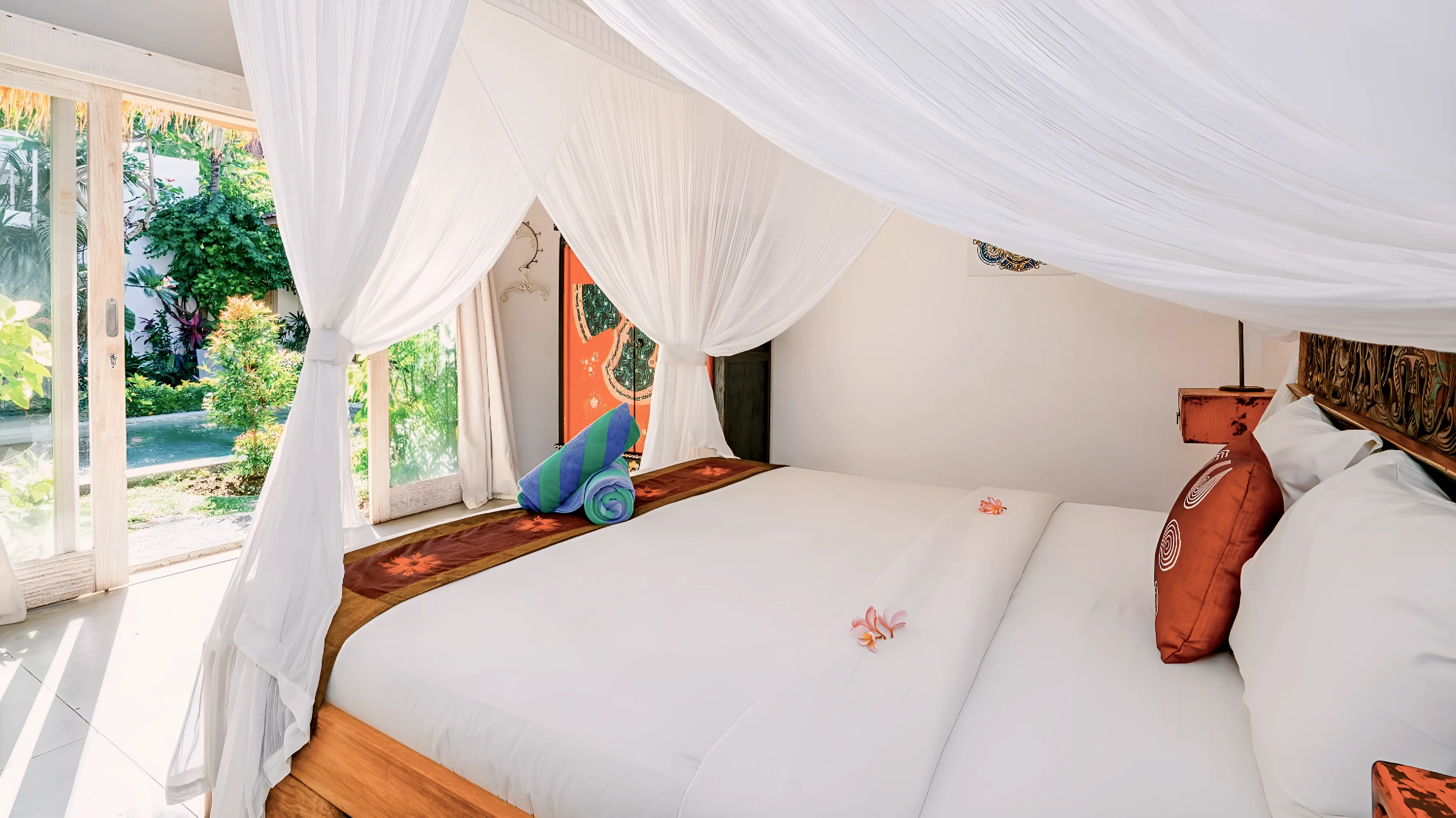 A four-poster bed with white netting, the garden through the window