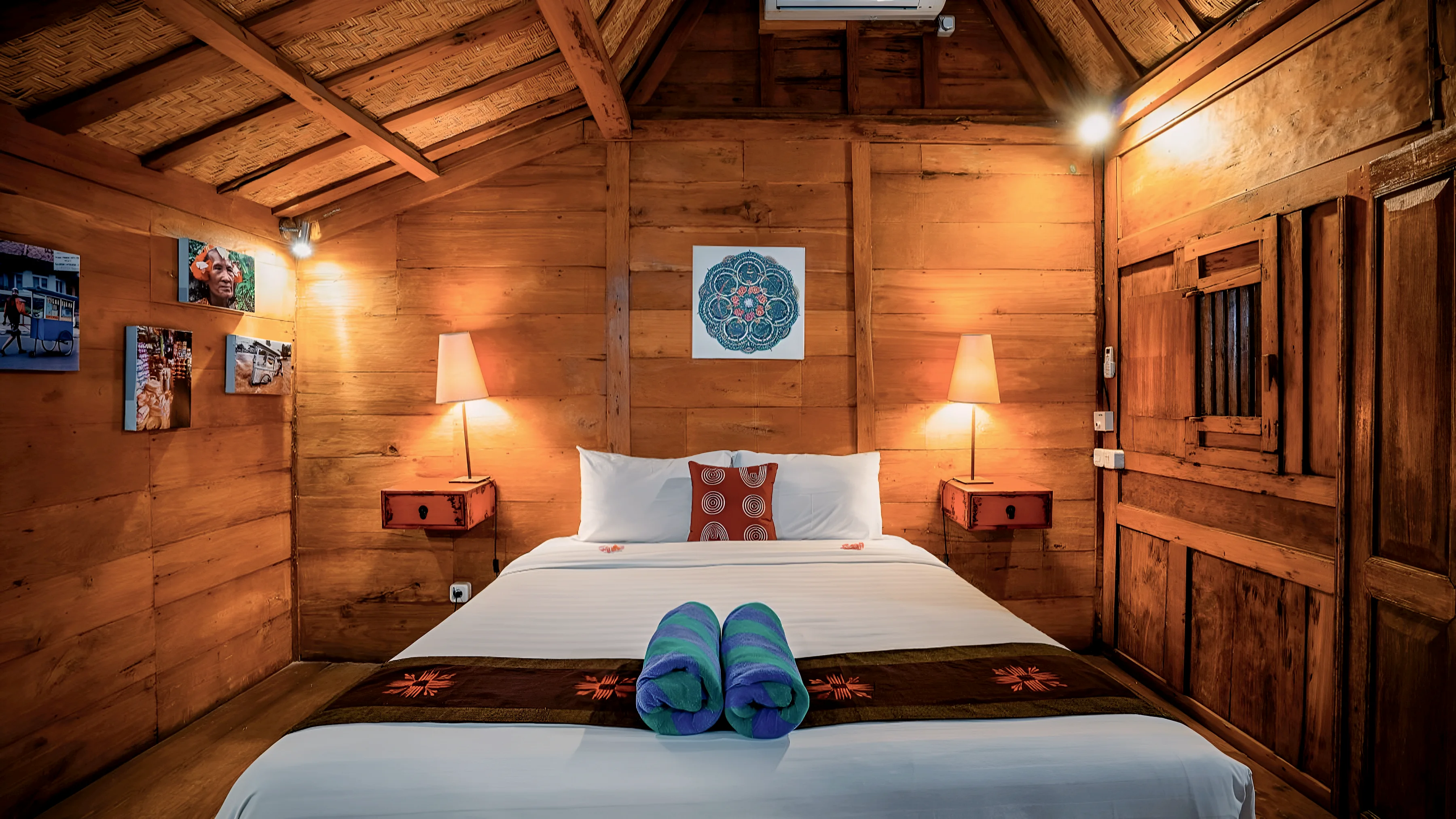 A Joglo bedroom in teak, a lamp on each side of the bed and a painted roundel above it