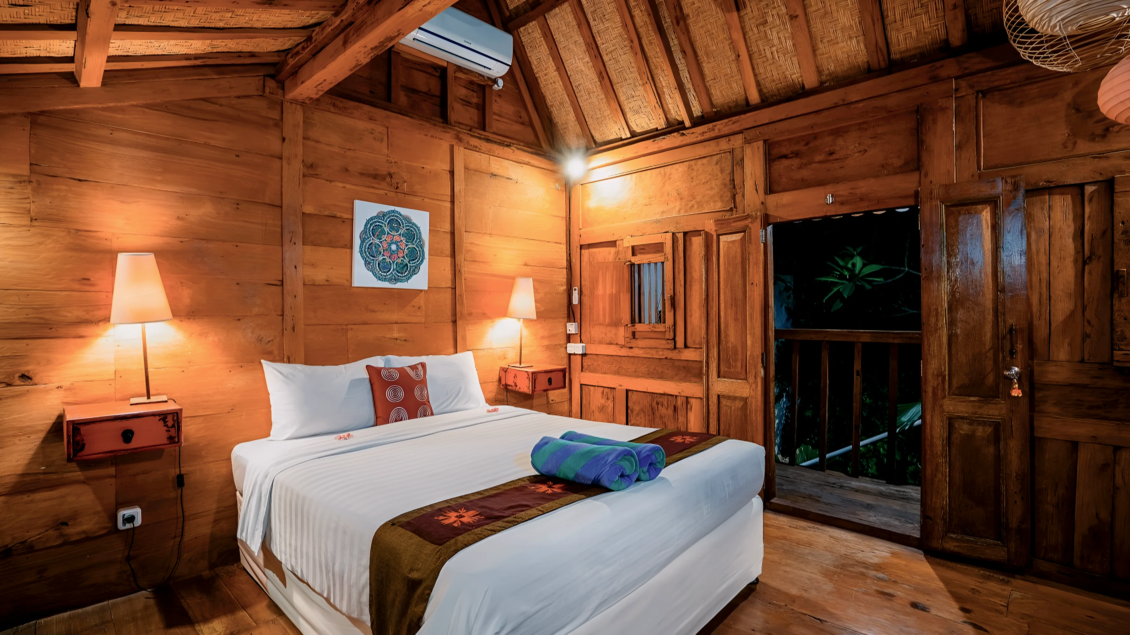 A Joglo bedroom with timber walls and a door open to a small balcony